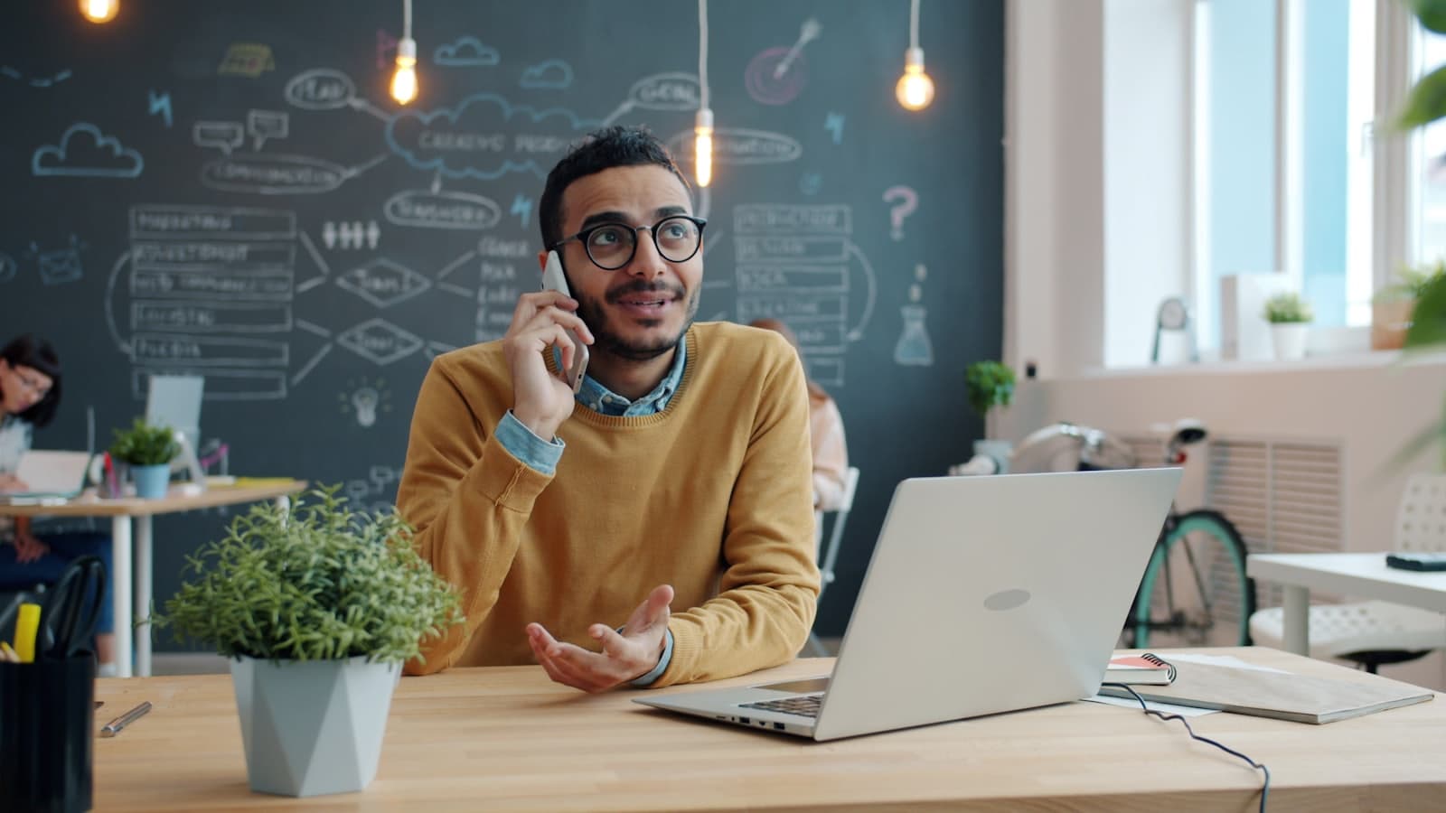 Someone taking a call on a mobile phone at their desk in an open-plan office.