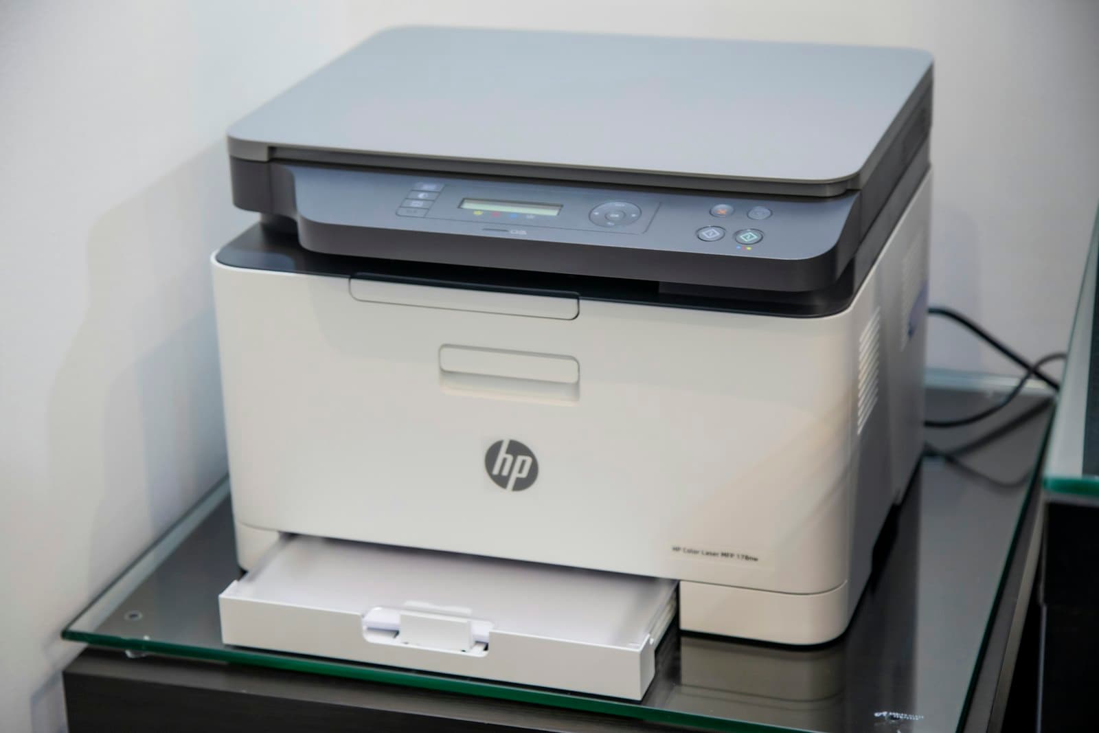 A white multifunction office printer on a glass stand.