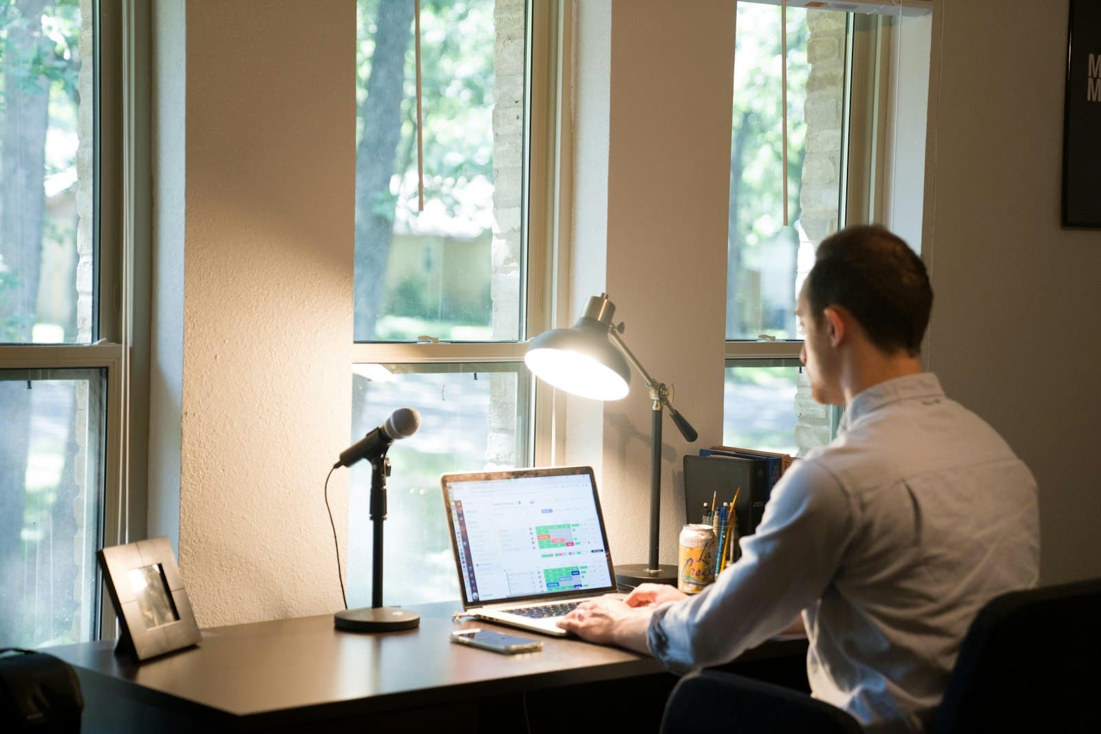 Someone working on a laptop at a desk by a window, seen from behind.