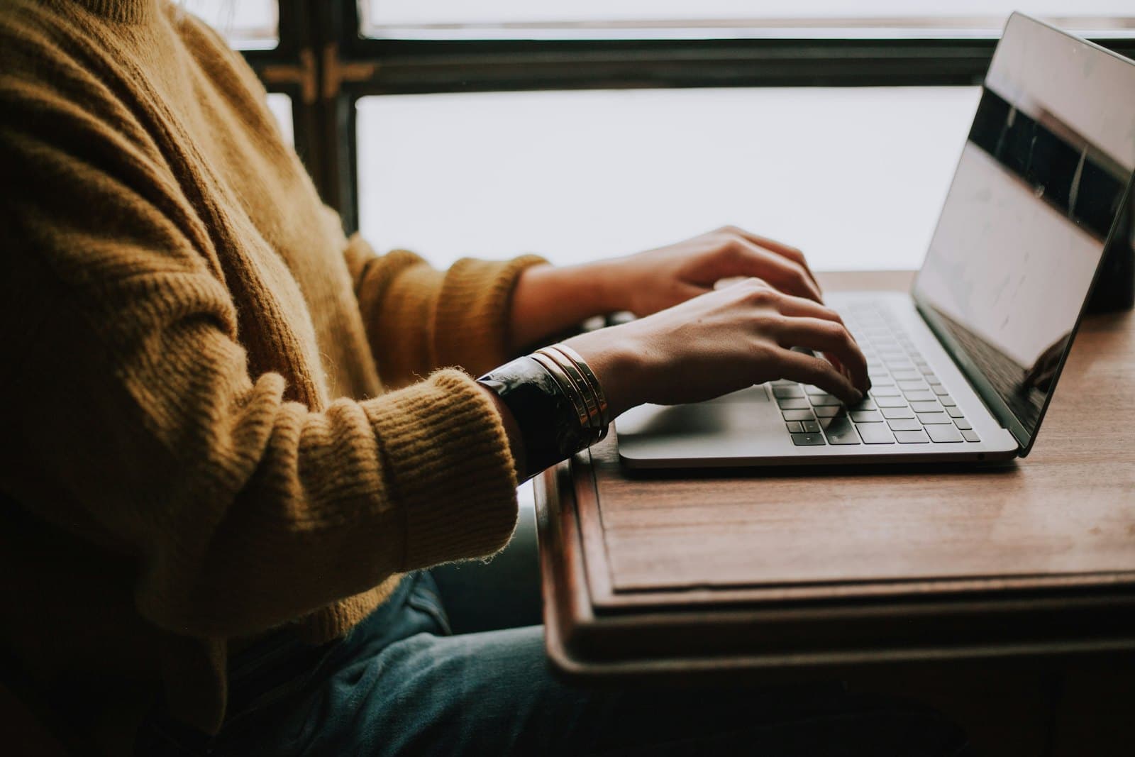 Hands typing on a laptop at a wooden desk, the screen turned away.