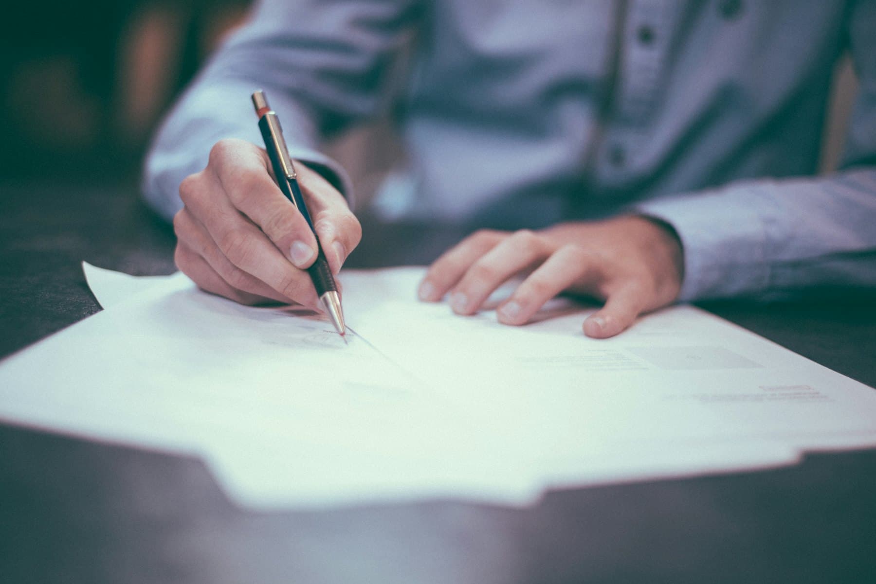Close-up of someone writing on a printed document at a desk with a pen.