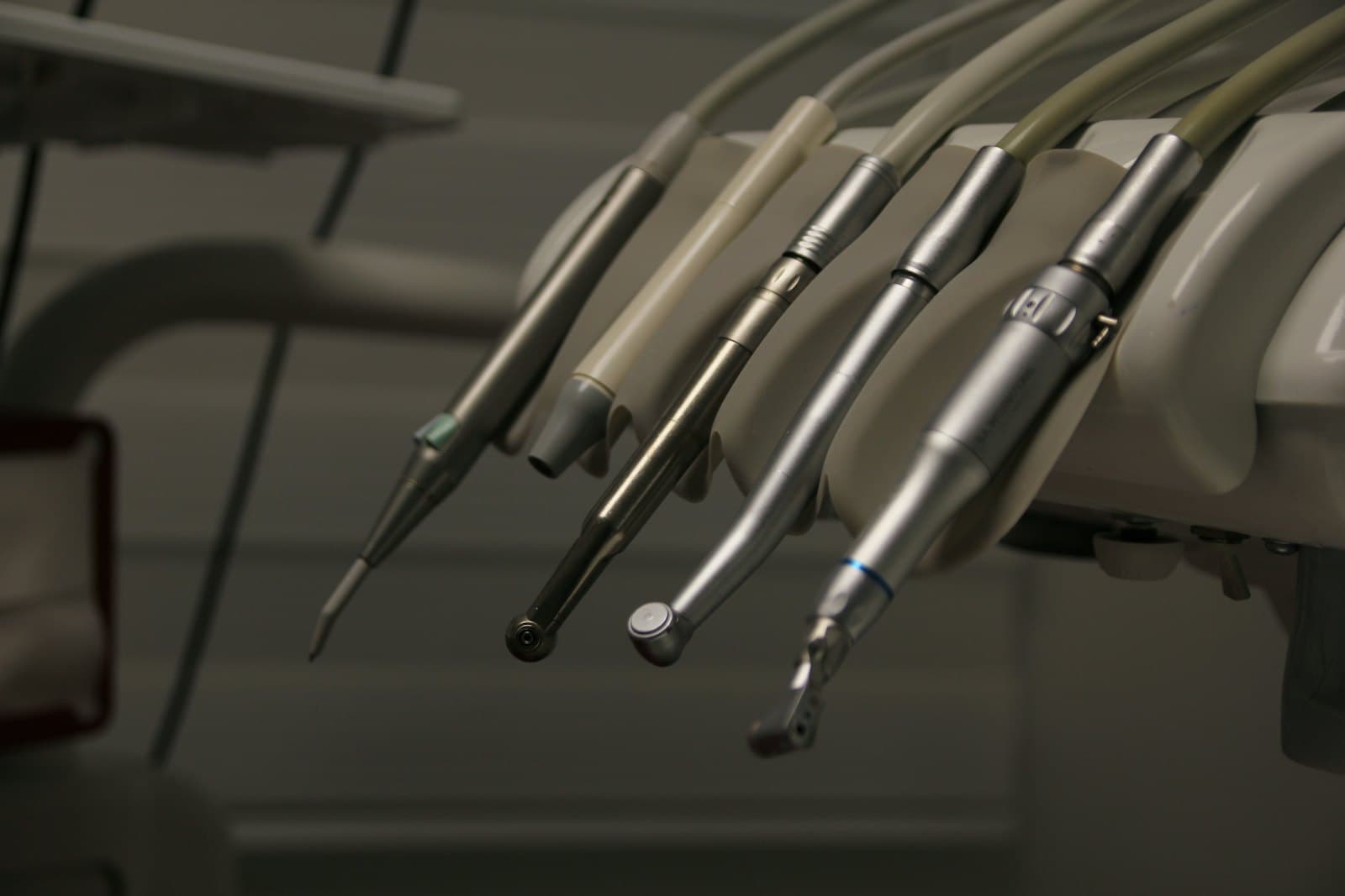 Dental handpieces resting in their holders on a treatment unit, in low light.