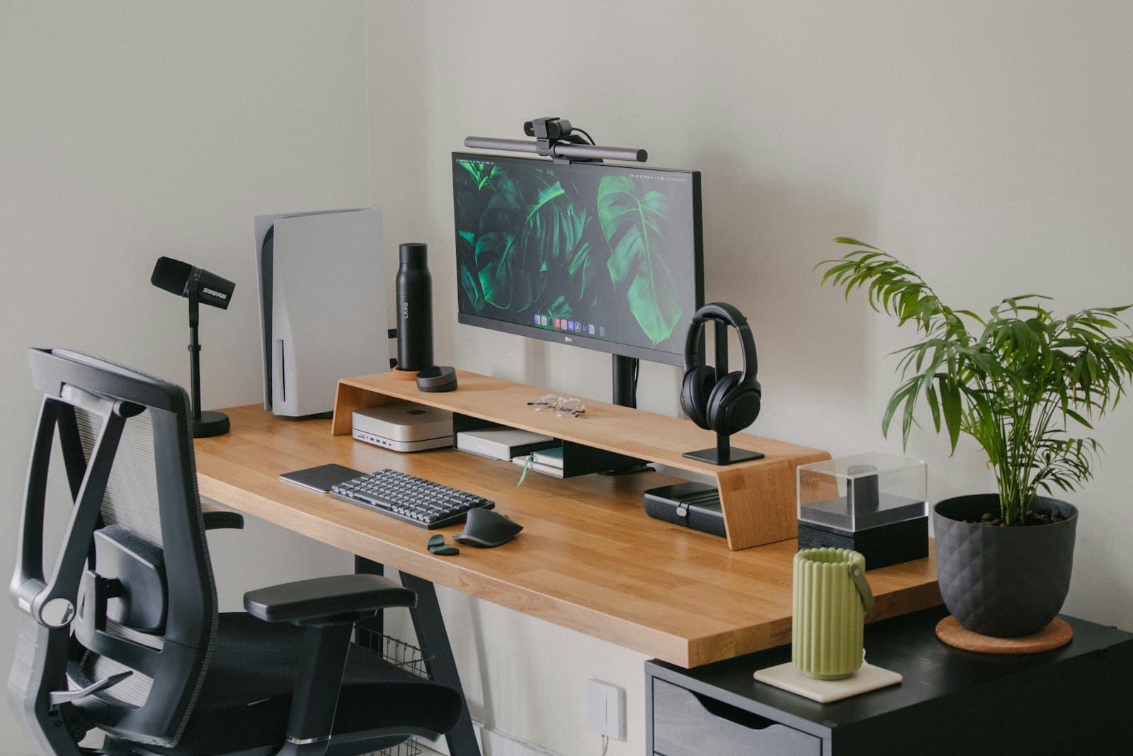 A tidy desk set up with a monitor, keyboard, headphones and a plant, ready for someone to sit down at.