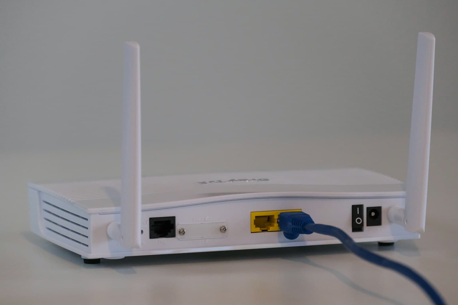 A white broadband router with its antennas up and an ethernet cable plugged into the back.